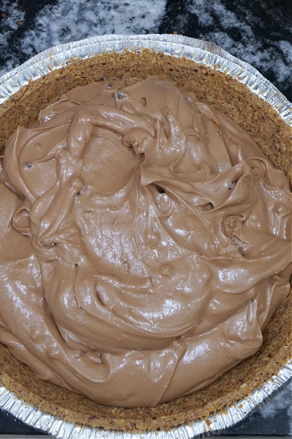 A premade pie crust with the chocolate cream pie mixture being spooned into the crust.