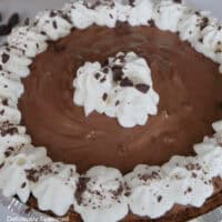 A white surface with a no bake chocolate cream pie on it that has whipped cream around the edge.