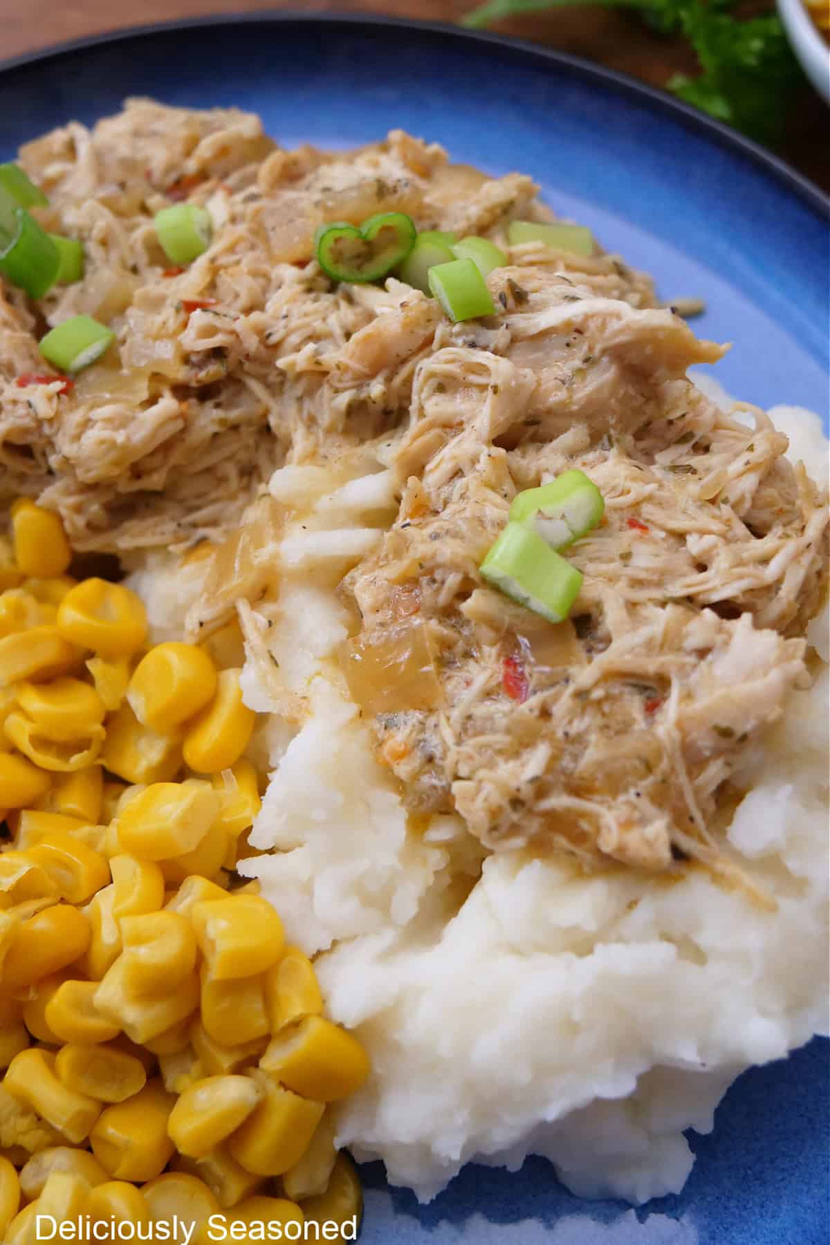 Mashed potatoes, corn, and shredded, slow cooked chicken on a blue plate.