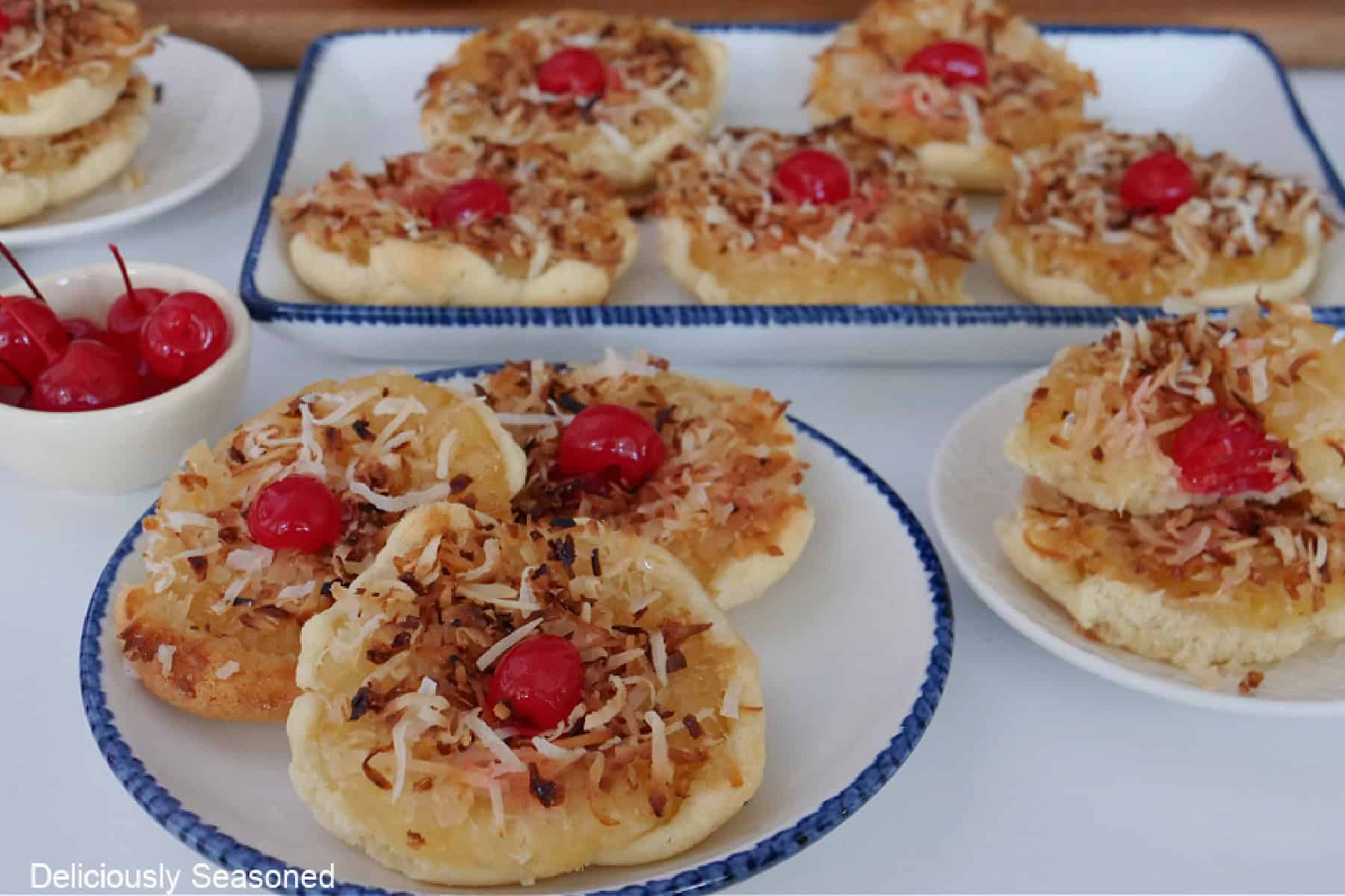 A white surface with white plates with blue trim with pineapple upside down cookies on each one.