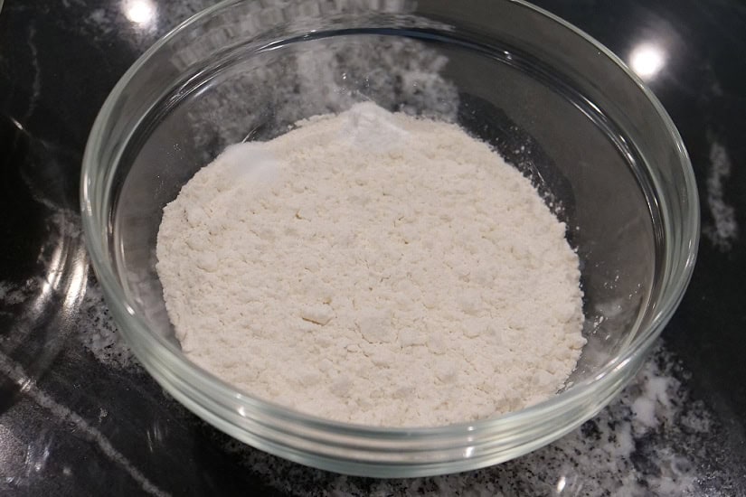 A black surface with a glass bowl filled with flour, baking powder, and salt.