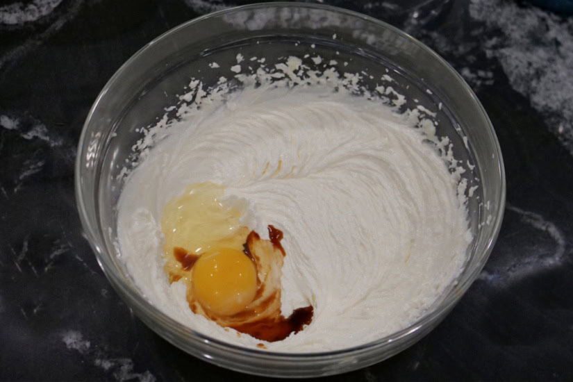 A black surface with a glass bowl with an egg and vanilla added to the wet ingredients.