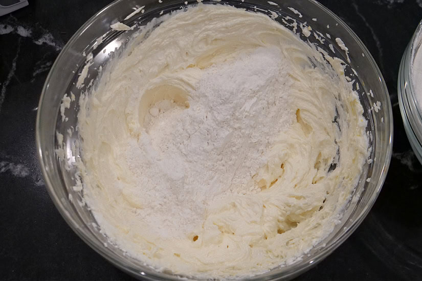 A black surface with a glass bowl with dry cookie ingredients added to wet cookie ingredients.