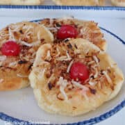 Three pineapple upside down sugar cookies on a white plate with blue trim.