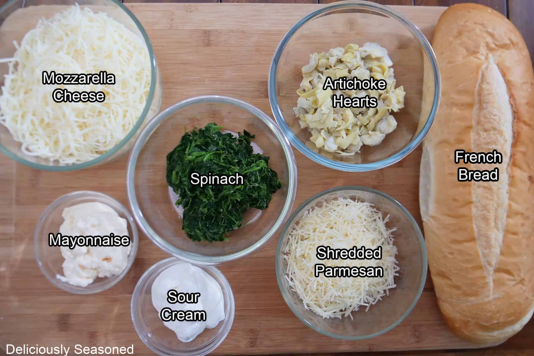 A wood surface with all the ingredients needed to make spinach artichoke cheese bread.