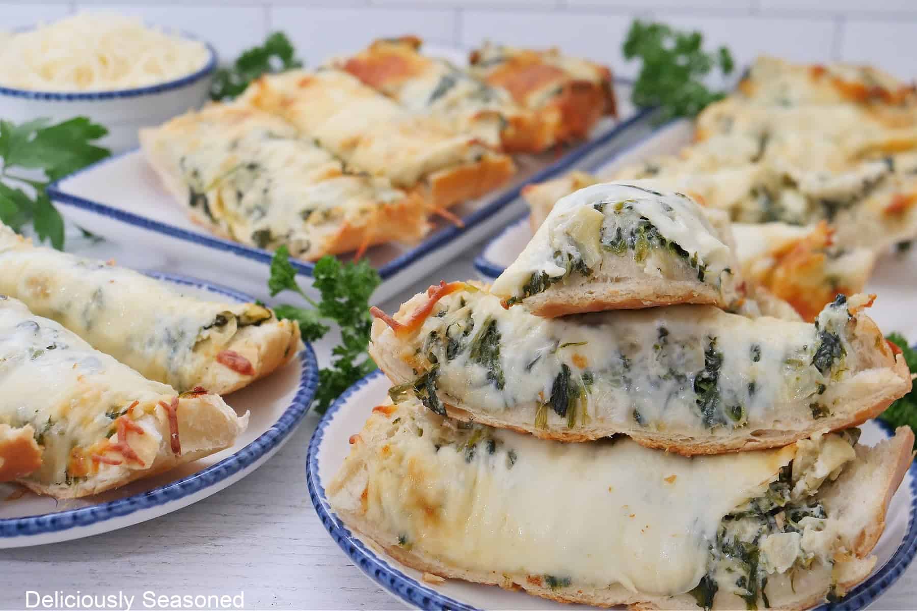 A white surface with French bread sliced into slices with spinach artichoke dip and mozzarella cheese covering the bread on each plate.