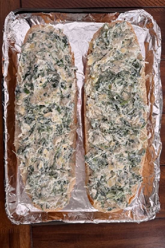 A foil lined baking sheet with French bread covered with spinach dip and mozzarella cheese.