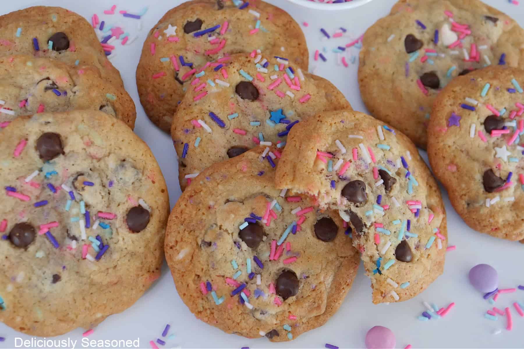 Chocolate chip cookies with spring colored sprinkles in them placed on a white surface.