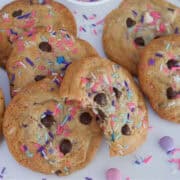A white surface with chocolate chip cookies with spring sprinkles in them.