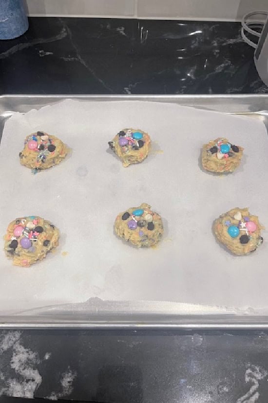 A parchment lined baking sheet with six cookie dough balls on it.