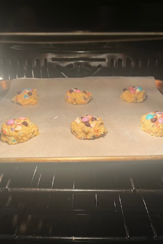 A baking sheet with six cookies on it baking in the oven.