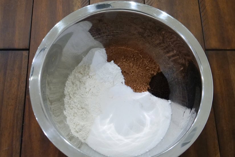 A silver mixing bowl with the dry chocolate cake ingredients in it.