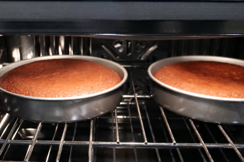 Two round cake pans in the oven baking two chocolate cakes.