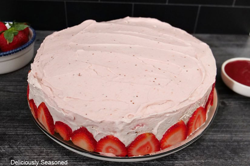 A grey surface with a frosted strawberry chocolate cake with sliced strawberries around the bottom edge.
