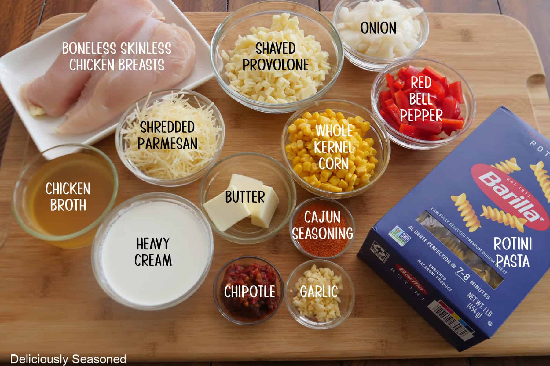 A wood surface with all the ingredients on it to make blackened chicken pasta.