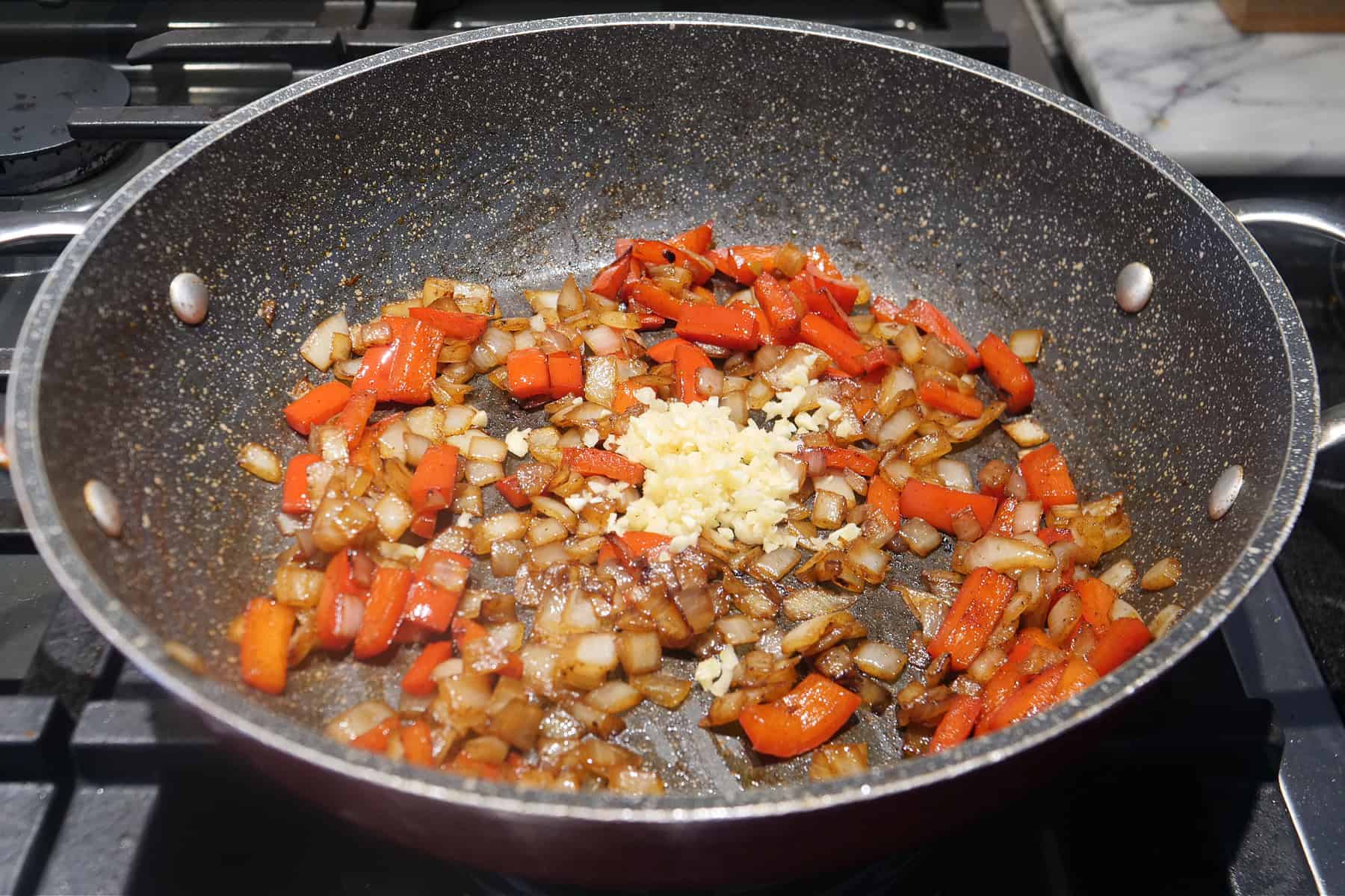 A skillet with diced onions, red bell pepper, and minced garlic in the pan.