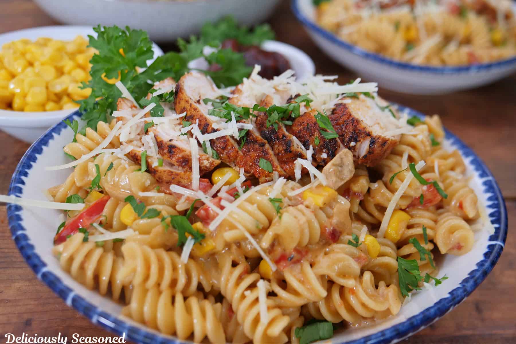 A wood surface with a white bowl with blue trim filled with blackened chicken pasta.