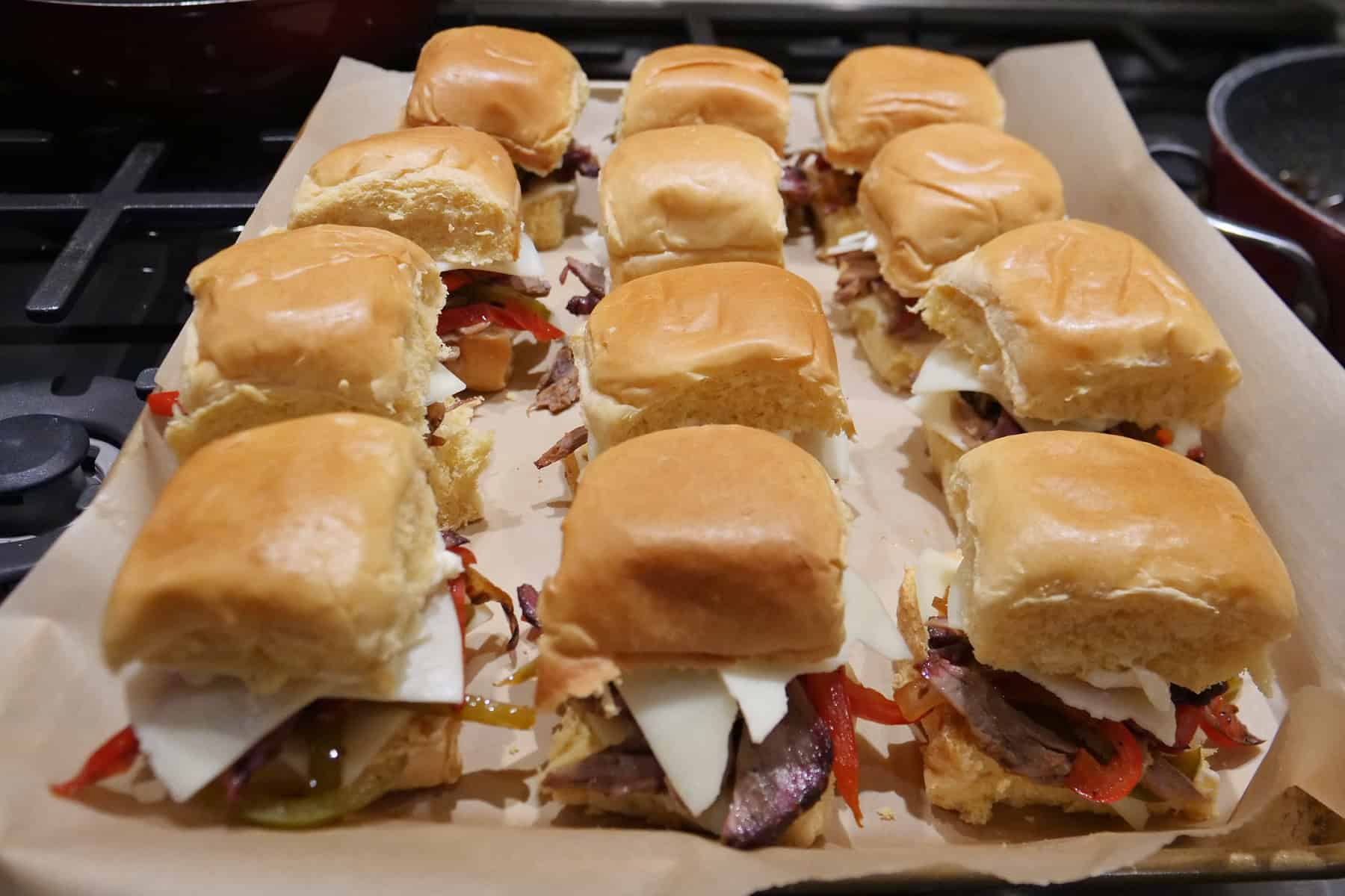 A baking sheet with twelve brisket philly sliders on it.