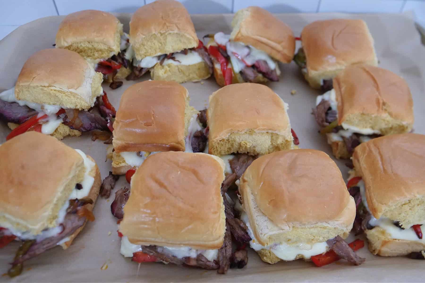 A baking sheet with brisket sliders right after being pulled from the oven showing the melty cheese.