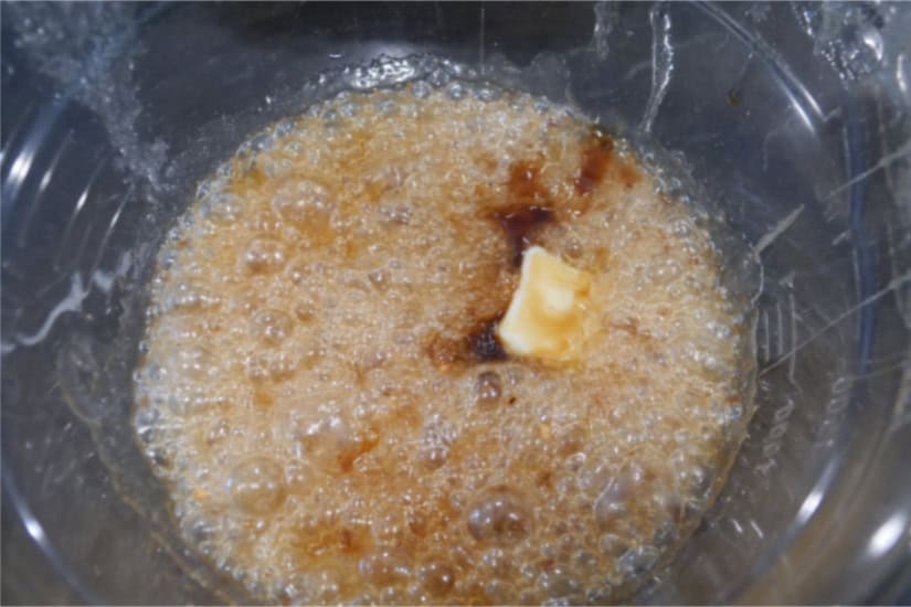 A glass bowl with vanilla and butter being added to the boiling sugar mixture.