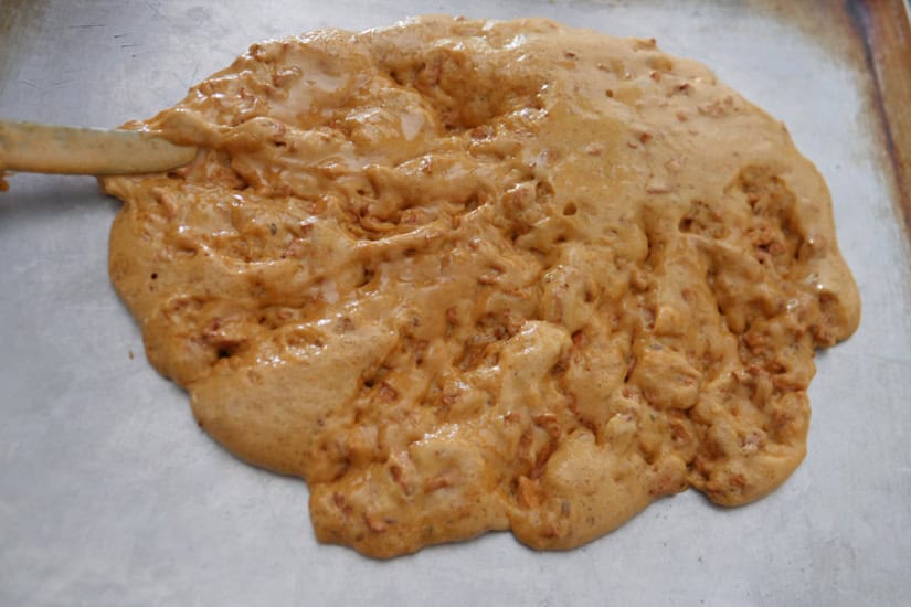 A silver baking sheet with hot cashew brittle being spread out to harden.
