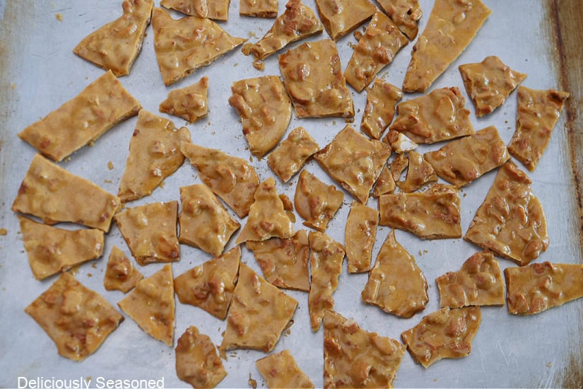 A silver baking sheet with hardened cashew brittle after it's been crack into little pieces.