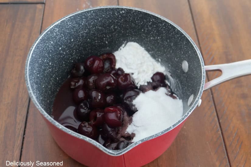 A saucepan with fresh cherries, sugar, lemon juice, cornstarch, and water in it.