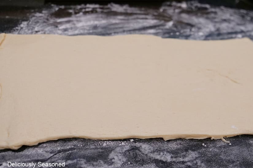 A black countertop with a crescent dough sheet rolled out on it.