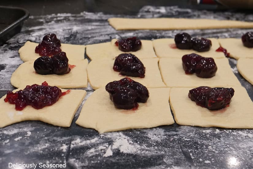 A black countertop with crescent sheets cut into 3 inch squares with cherry filling on them.