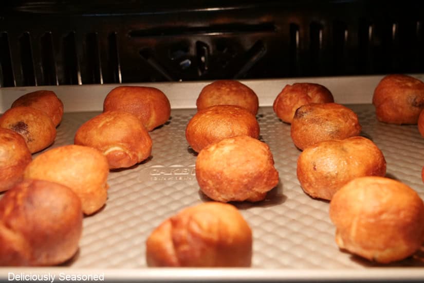 A baking sheet with mini cherry pie bombs on it baking in the oven.
