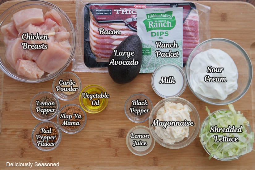 A wood surface with all the ingredients on it to make chicken bacon ranch sliders with avocado ranch dressing.