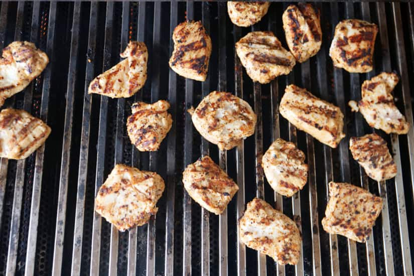 Grill grates with pieces of grilled chicken on it.