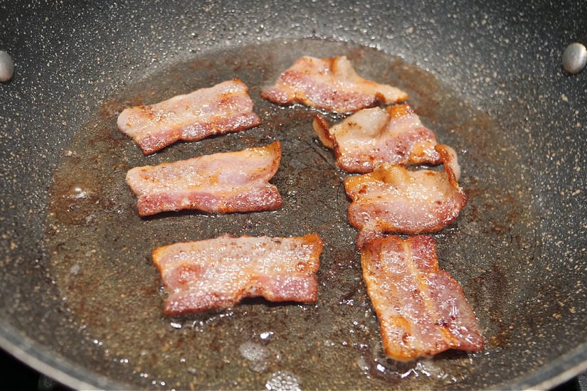 A frying pan with pieces of bacon being fried.