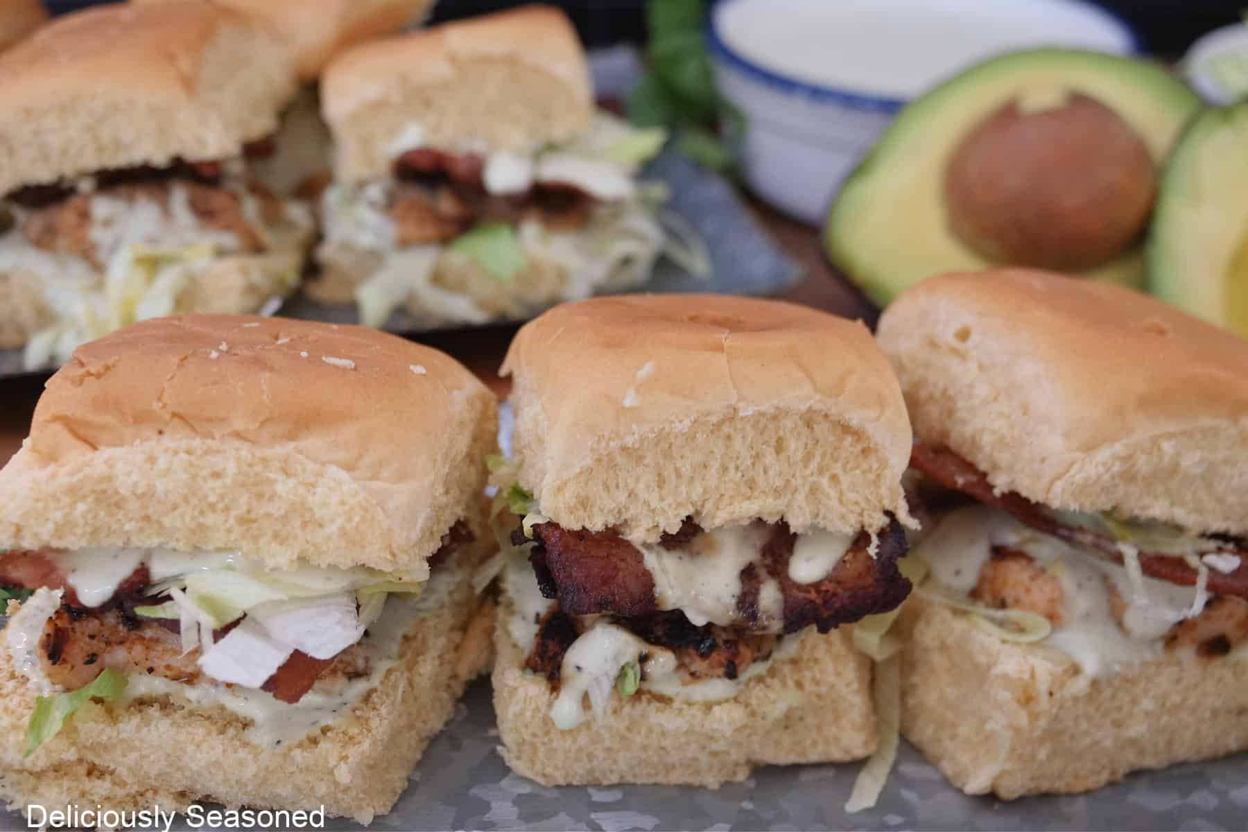 Three chicken bacon ranch sliders on a silver tray with more sliders in the background.