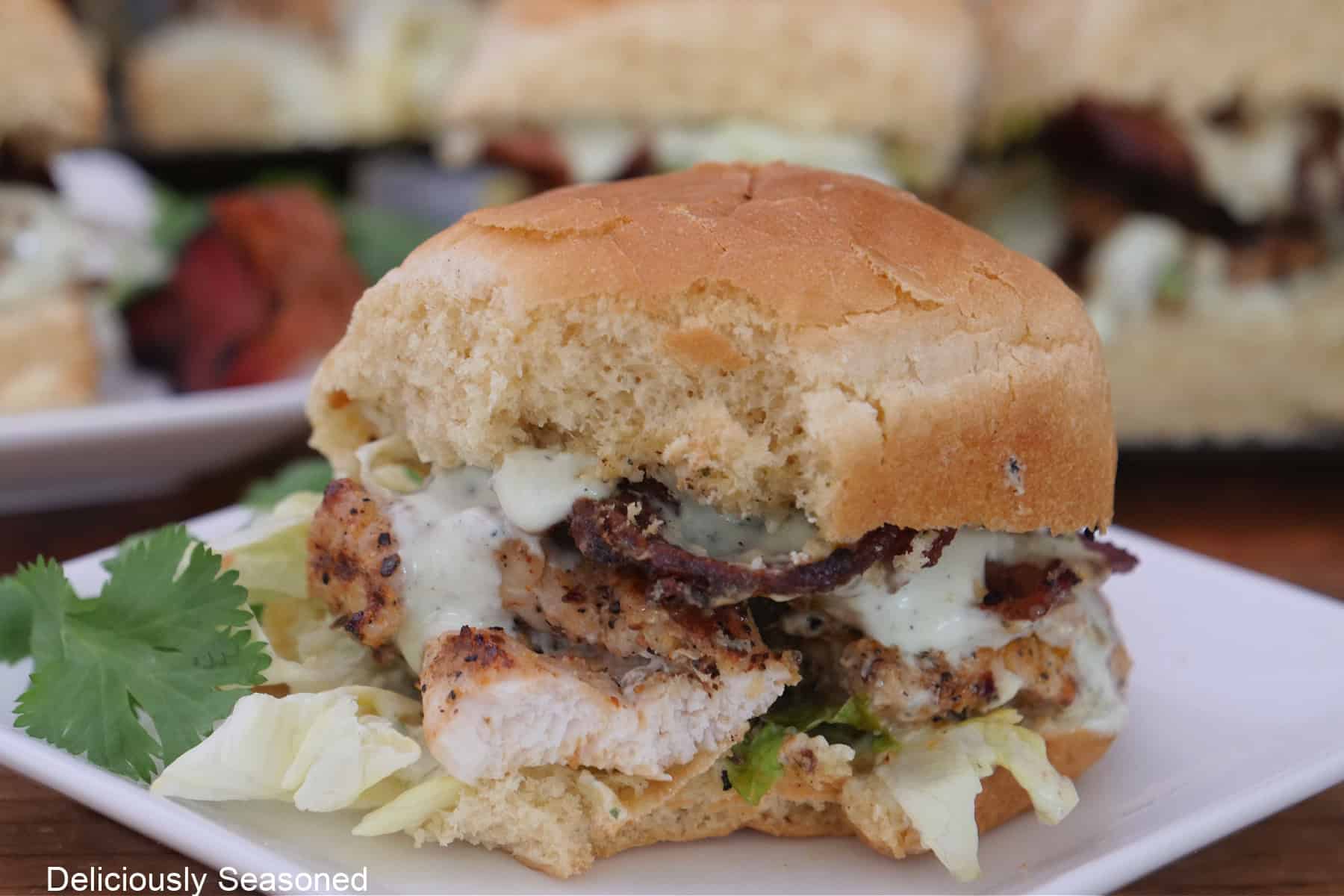 A white small square plate with a chicken slider on it and more sliders in the background.