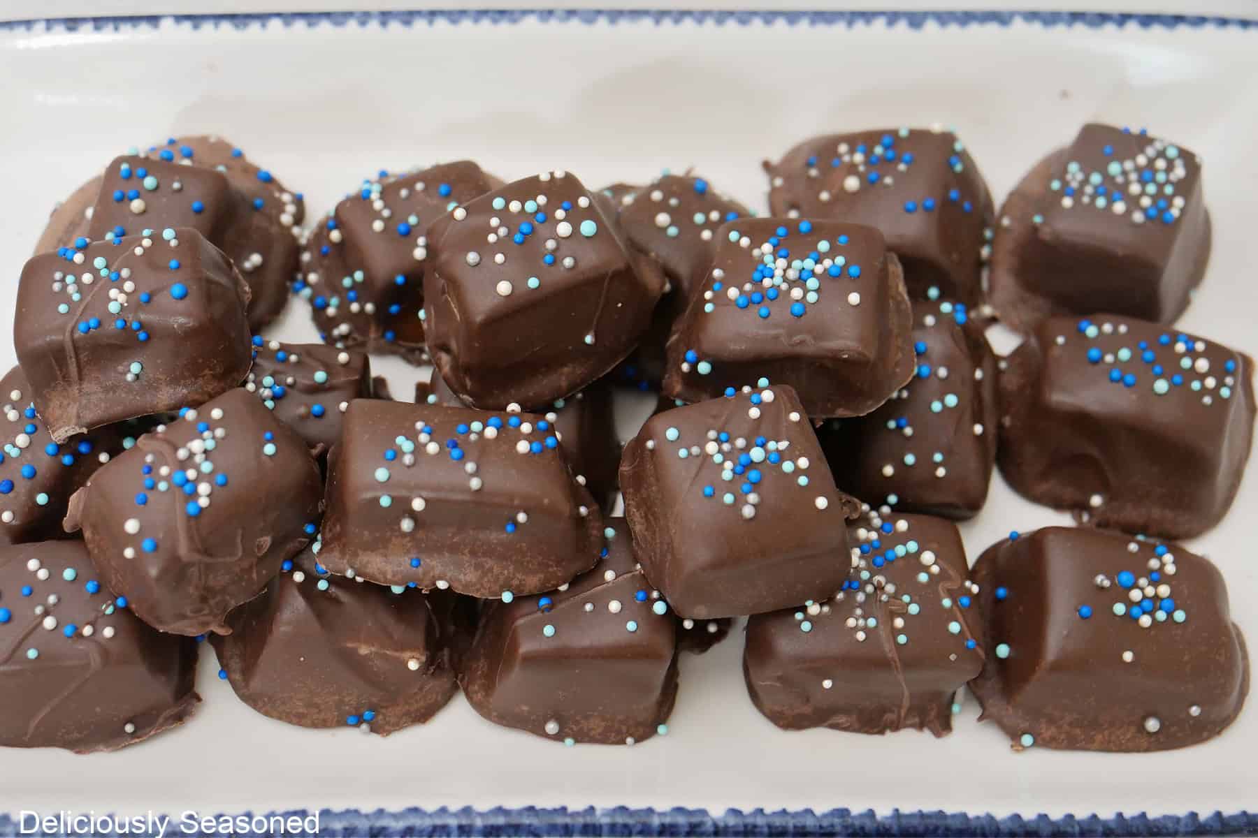 A white oblong plate with blue trim with a over a dozen pieces of chocolate covered caramels on it.