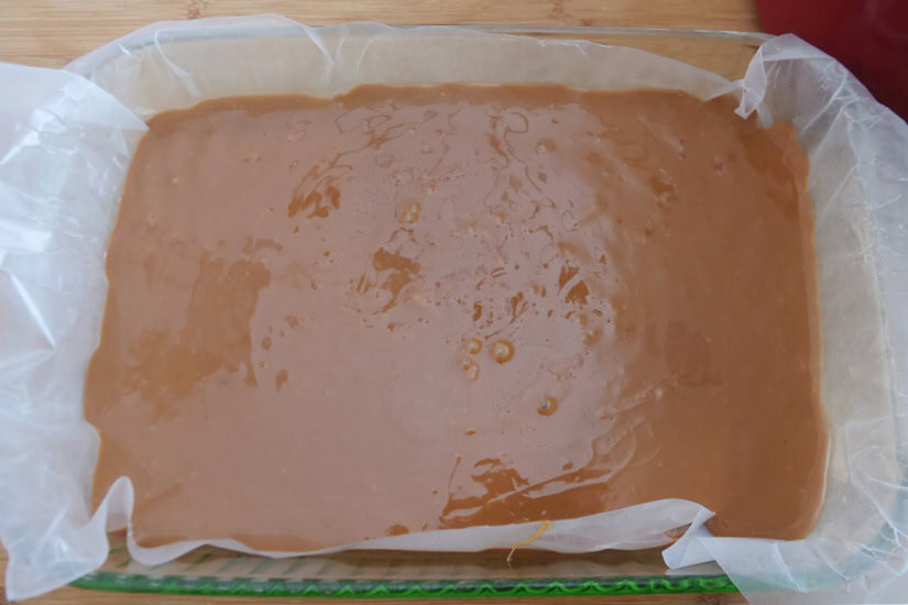A glass 9x13 baking dish with caramel pour into it over the parchment paper that lines to dish.