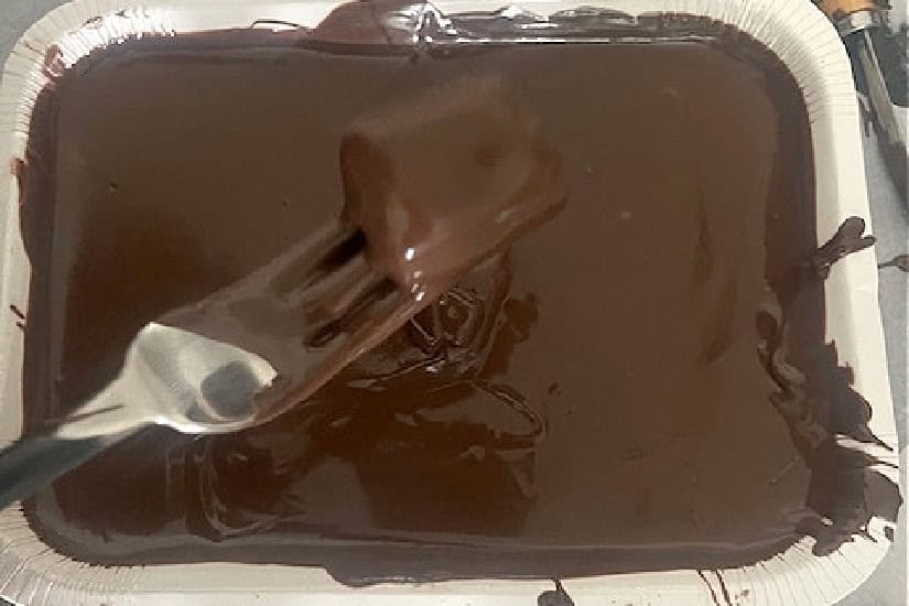 A piece of caramel being dipped in melted chocolate.