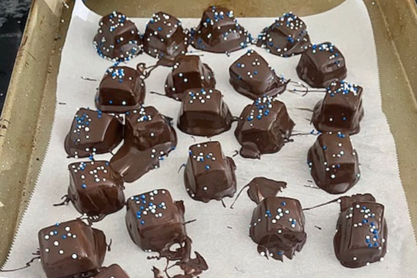 A parchment lined baking sheet with chocolate dipped caramels on it sprinkled with candy sprinkles.