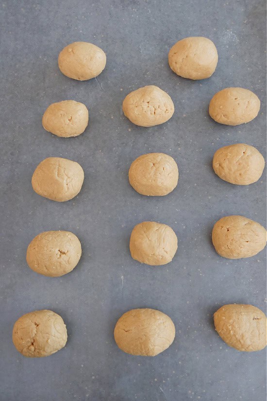 A baking sheet lined with parchment paper with 14 mini dough eggs on it.