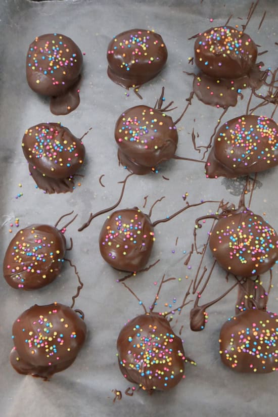 A parchment lined baking sheet with twelve chocolate covered mini cookie butter eggs with sprinkles on top.