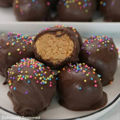 A small white plate with black trim with six mini cookie butter Easter eggs on it with a bite taken out of the one on top.