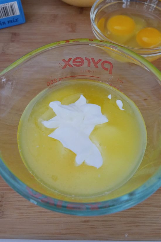 A wood surface with a glass bowl with melted butter and sour cream in it before being mixed together.