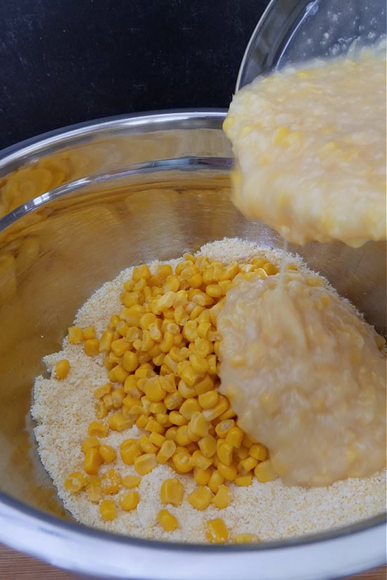 A sliver mixing bowl with cornbread mix, corn, and cream corn being added.