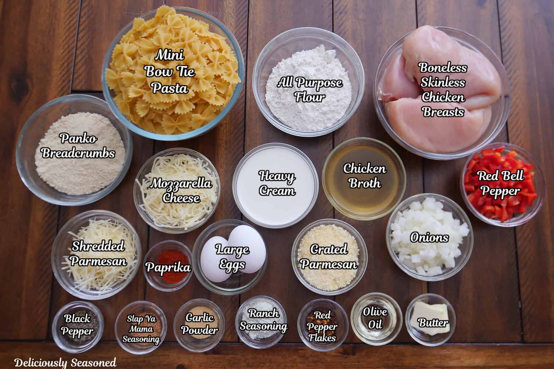 A brown table top with all the ingredients in glass bowls to make Parmesan crusted chicken casserole.