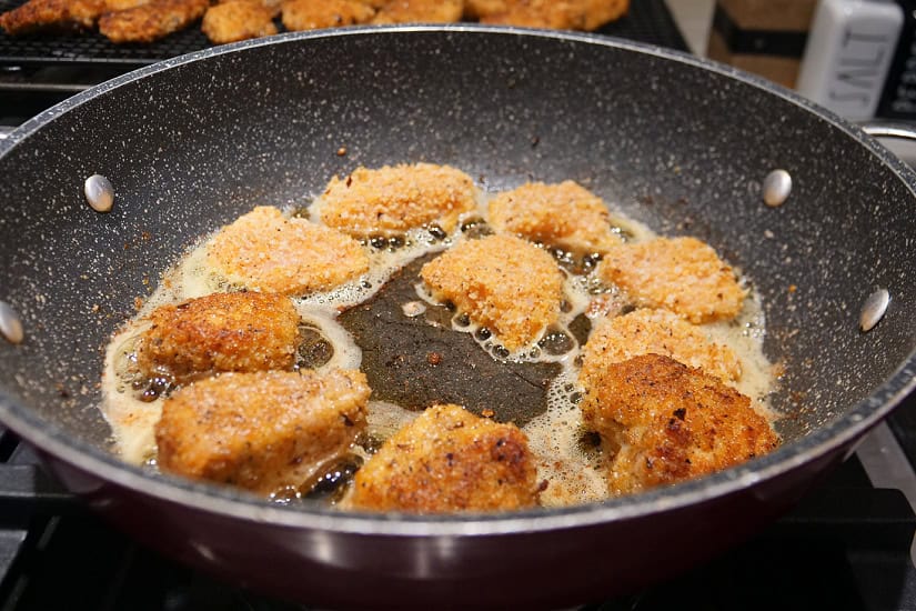 A frying pan with 10 bite-size pieces of coated chicken being fried to golden perfection.