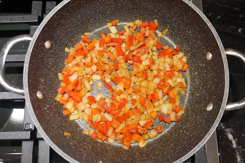 A pan with sauteed onions and red bell pepper in it.