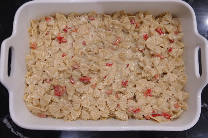 A white 9 by 13 baking dish with a layer of pasta and cream sauce mixed together.