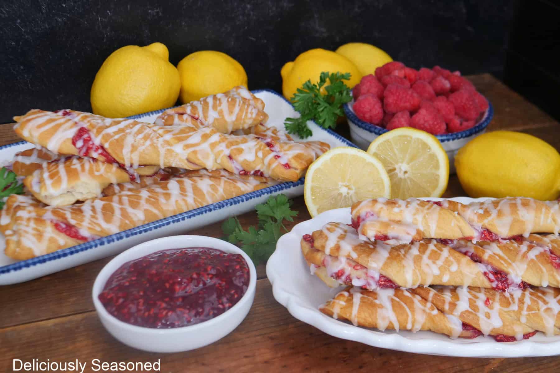 A wood surface with two white plate with blue trim with raspberry twists on them with lemons and raspberries in the background.