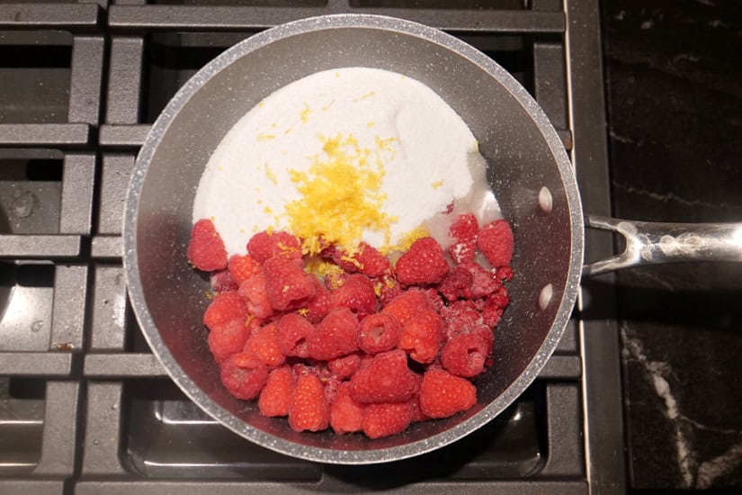 A saucepan with fresh raspberries, sugar, lemon juice and lemon zest in it.